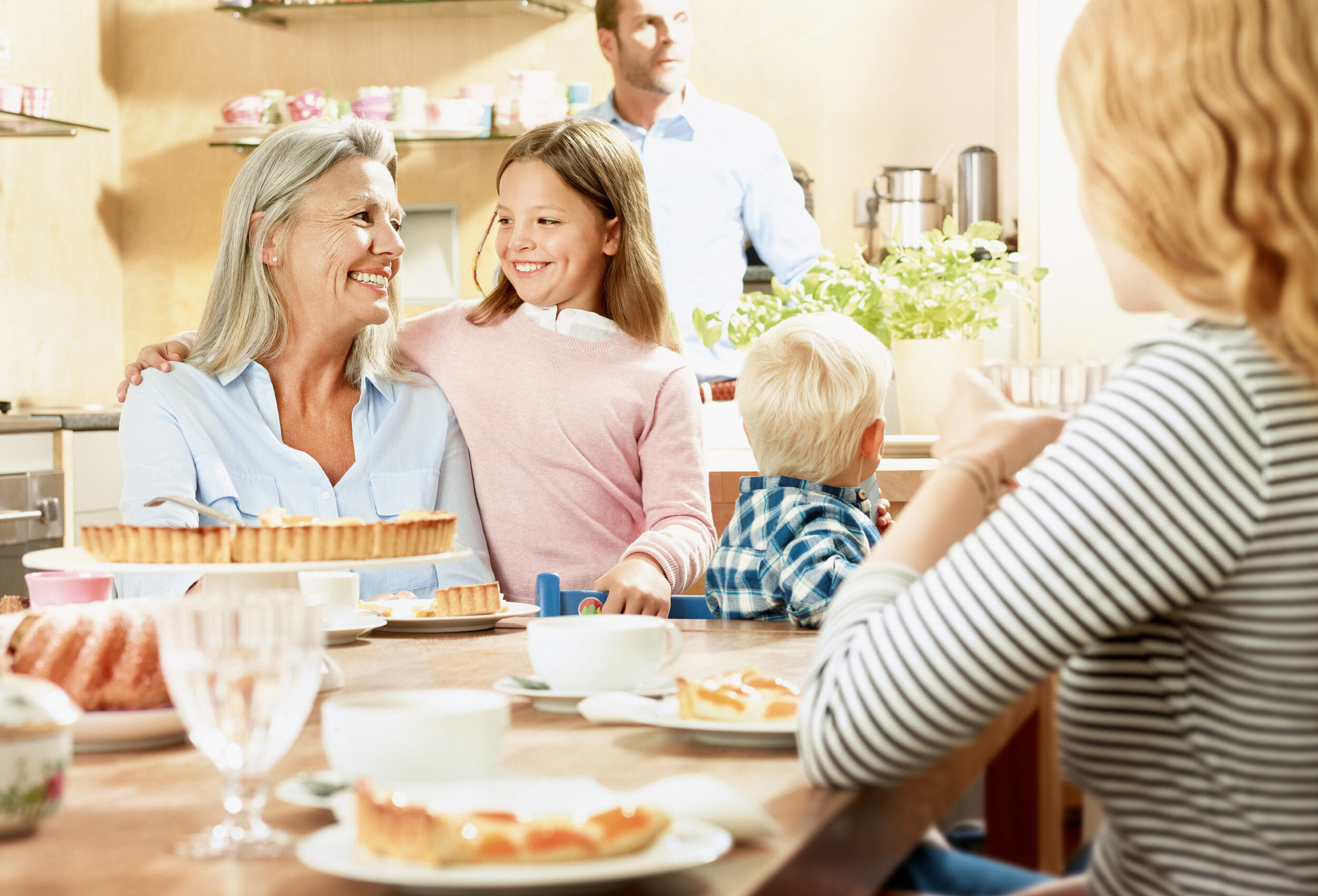 Eine Familie sitzt zusammen am Frühstückstisch. Zu sehen sind Oma und ein Kind und der Vater im Hintergrund.